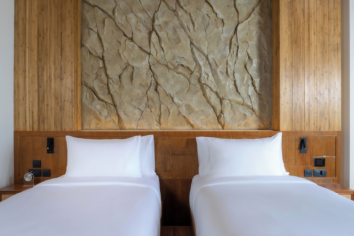 Een hotelkamer met twee bedden, een houten hoofdbord, een stenen muur en bedbedieningen.