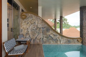 A pool area with stone walls, wooden chairs, and a view of buildings and trees. - Sinae Phuket Luxury Hotel (Ratsada)
