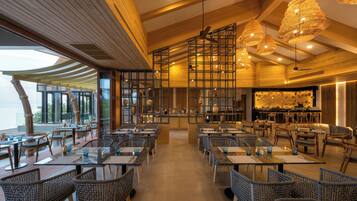 L’intérieur d’un restaurant se caractérise par de hauts plafonds, des poutres en bois et différents types d’aménagements, notamment des tables et des chaises en osier.