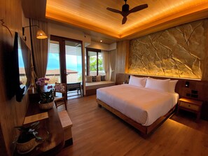Een hotelkamer met een groot bed, een plafondventilator, uitzicht op de oceaan en een stenen muur.