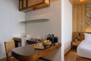 A compact hotel room with a wooden dining table, a bed, a nightstand, and a wall-mounted shelf. - Sinae Phuket Luxury Hotel (Ratsada)