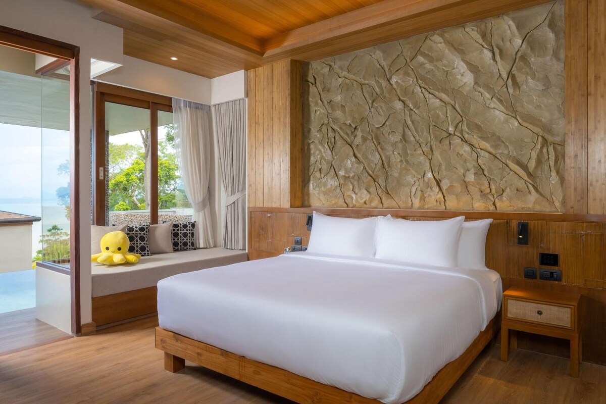 Een moderne hotelkamer met een groot bed, een accentmuur van steen, een raam met uitzicht en een houten plafond.