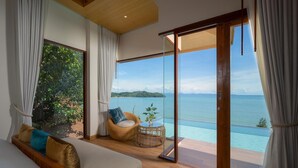 Une chambre avec un lit, un fauteuil en osier et une vue sur la mer.
