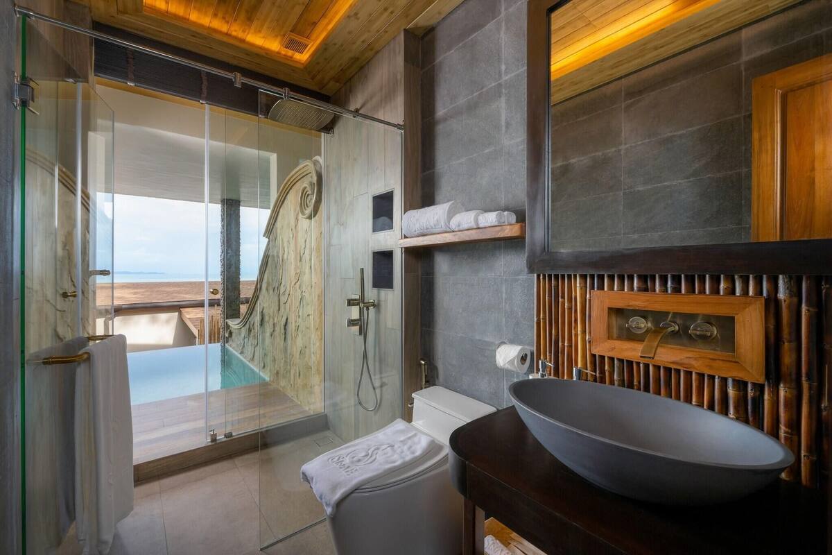 Een badkamer met een douchecabine van glas, een groot wastafelmeubel en uitzicht op zee.
