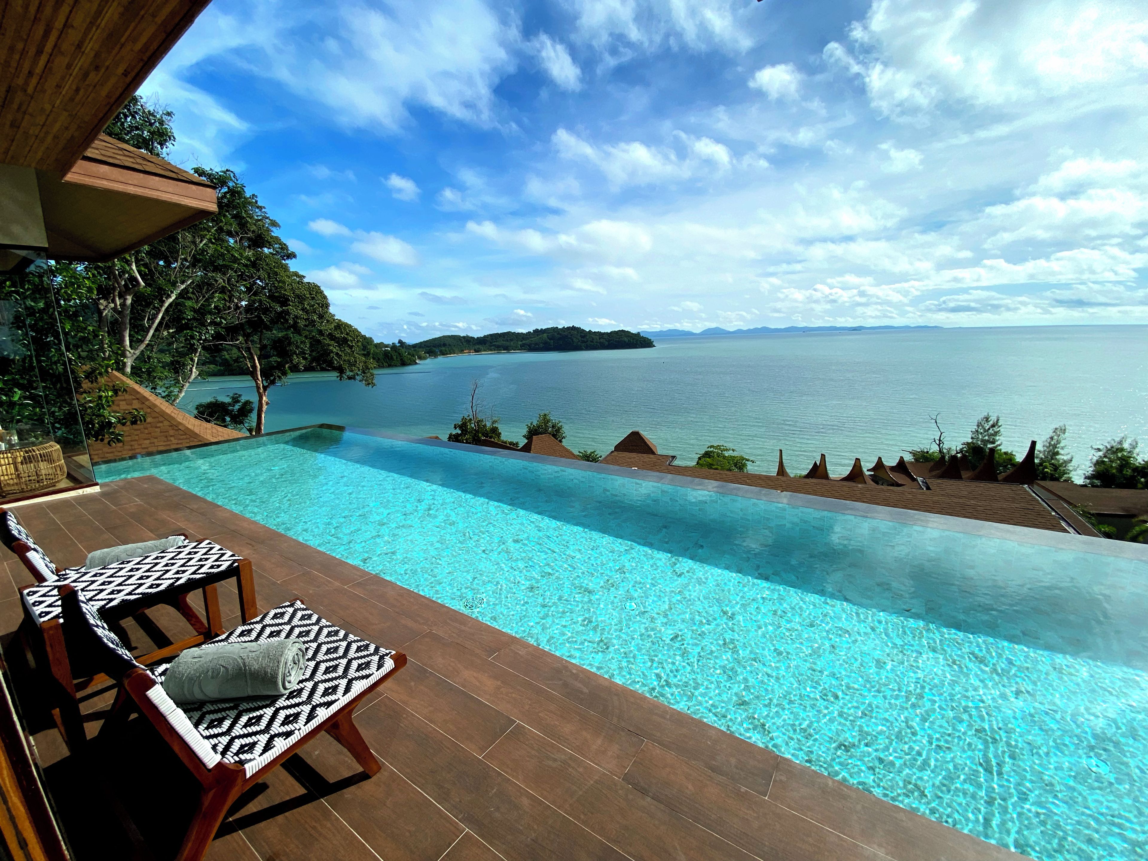 Ein unendlicher Pool mit Blick auf ein großes Gewässer und die ferne Landschaft.