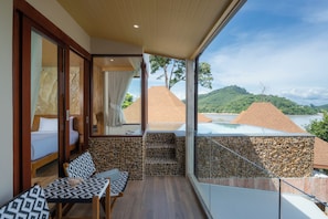 A balcony with a stone wall, a bed, a table with patterned cushions, and a view of a mountainous landscape. - Sinae Phuket Luxury Hotel (Ratsada)