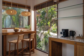 Cuina amb cafetera, cistella i finestra amb vista a vegetació.