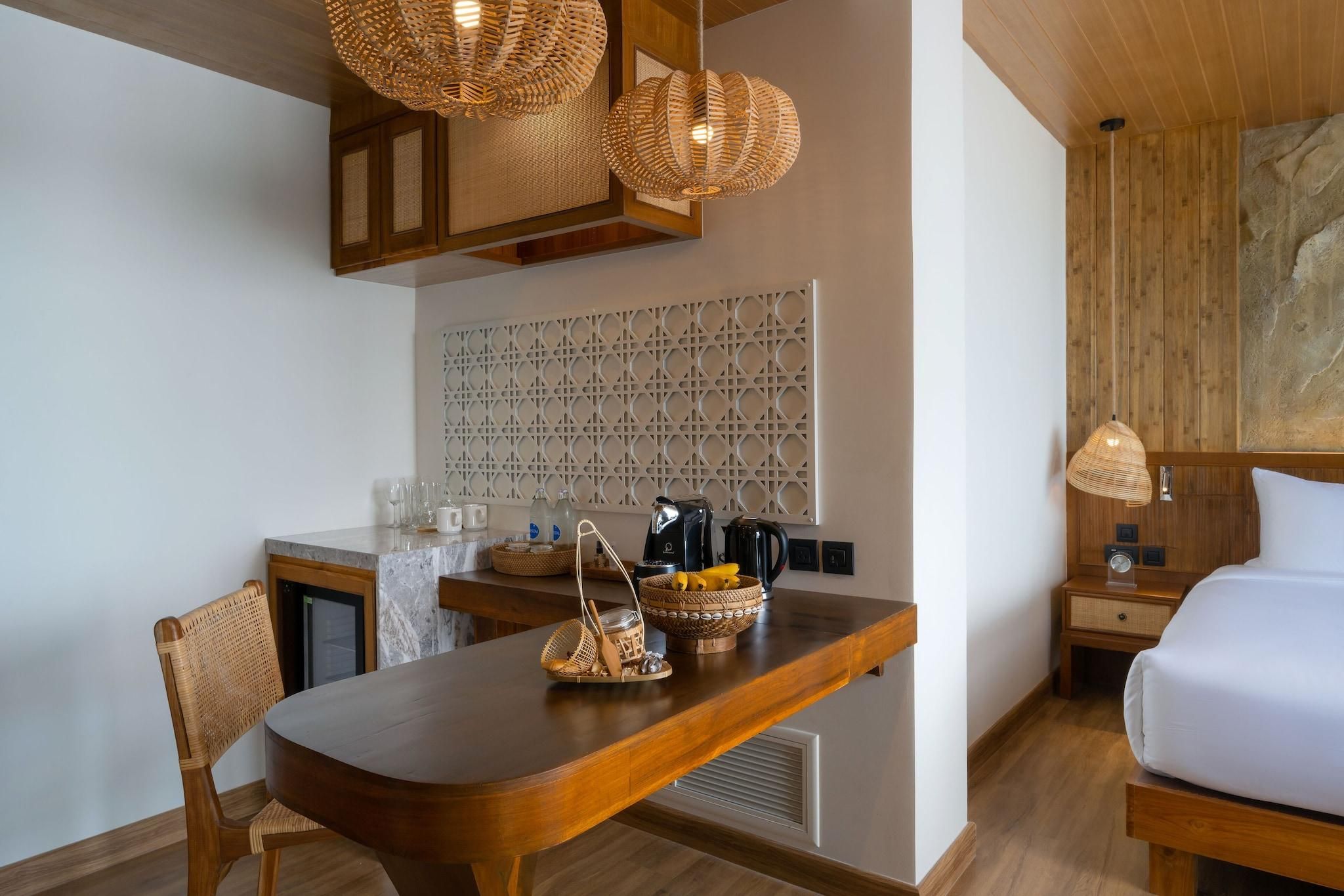 A compact room with a wooden dining table, a white bed, and a kitchenette area.