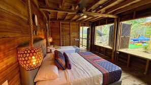 A wooden cabin with two beds, a hanging light fixture, and a view of the outdoors.
