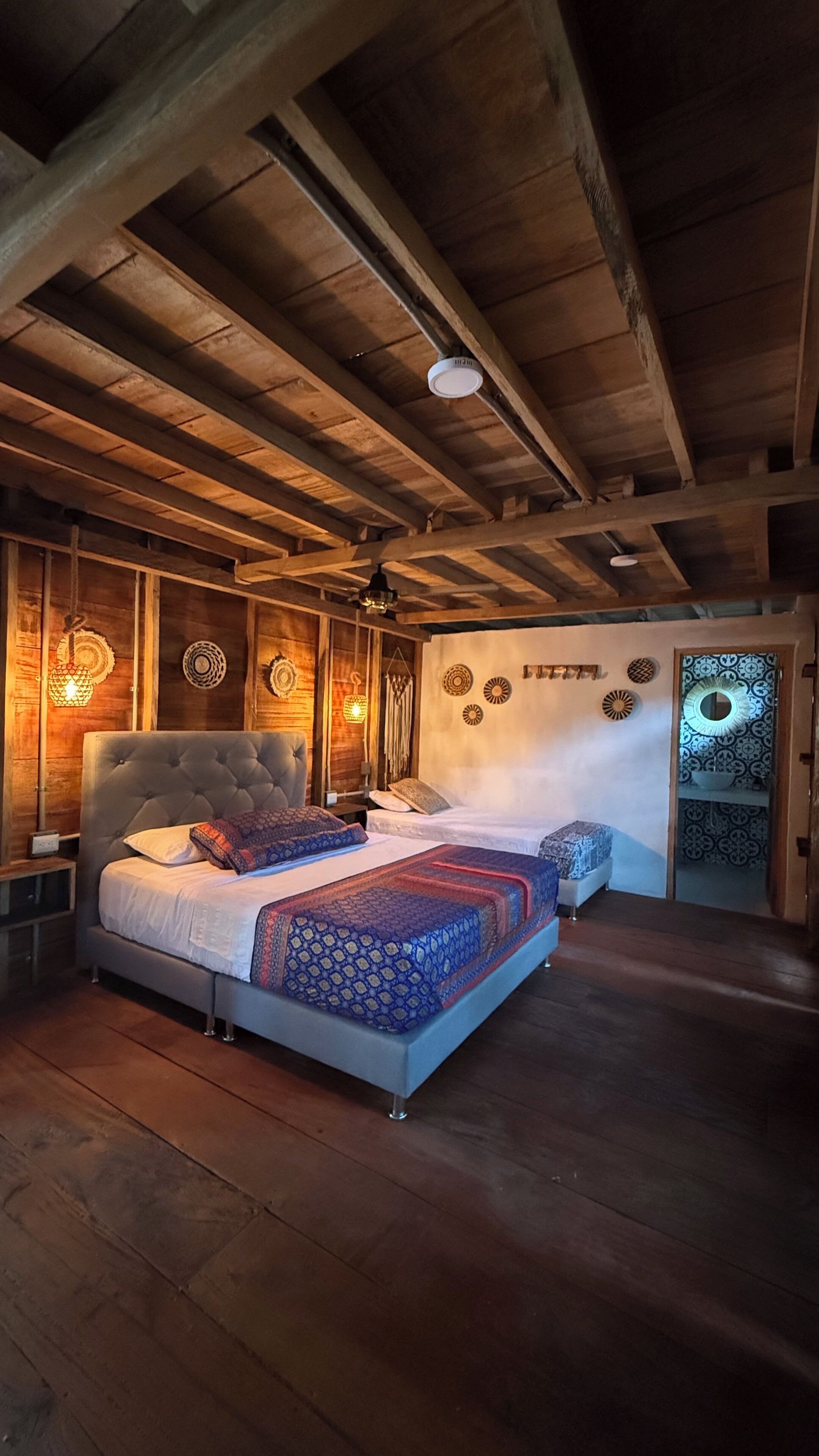 A bedroom with a large bed, wooden ceiling beams, and wall-mounted decorative lights.