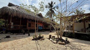 A wooden house with a thatched roof, surrounded by gravel and small plants.