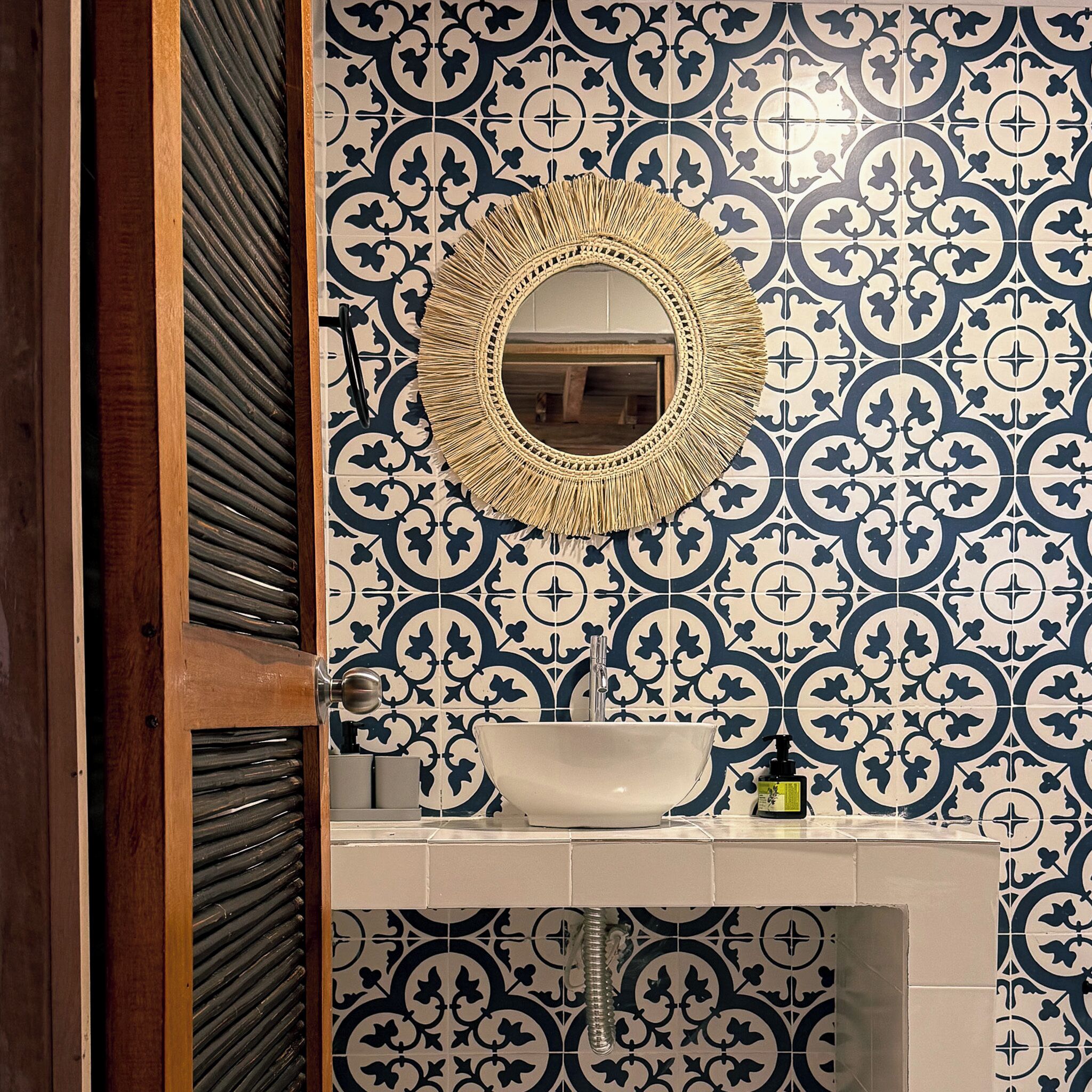 A bathroom with a patterned tile wall, a round mirror, and a sink.