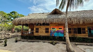A wooden house with a thatched roof, a balcony, and a colorful door. - RINCON DEL MANGLE (San Onofre)