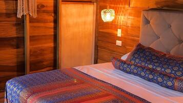 A wooden cabin room with a bed, macrame wall hanging, and a wall-mounted light fixture.