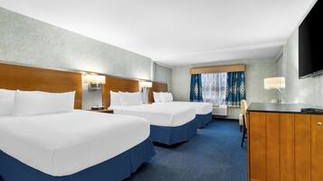 A hotel room with three beds, a desk, a TV, and a window with curtains.