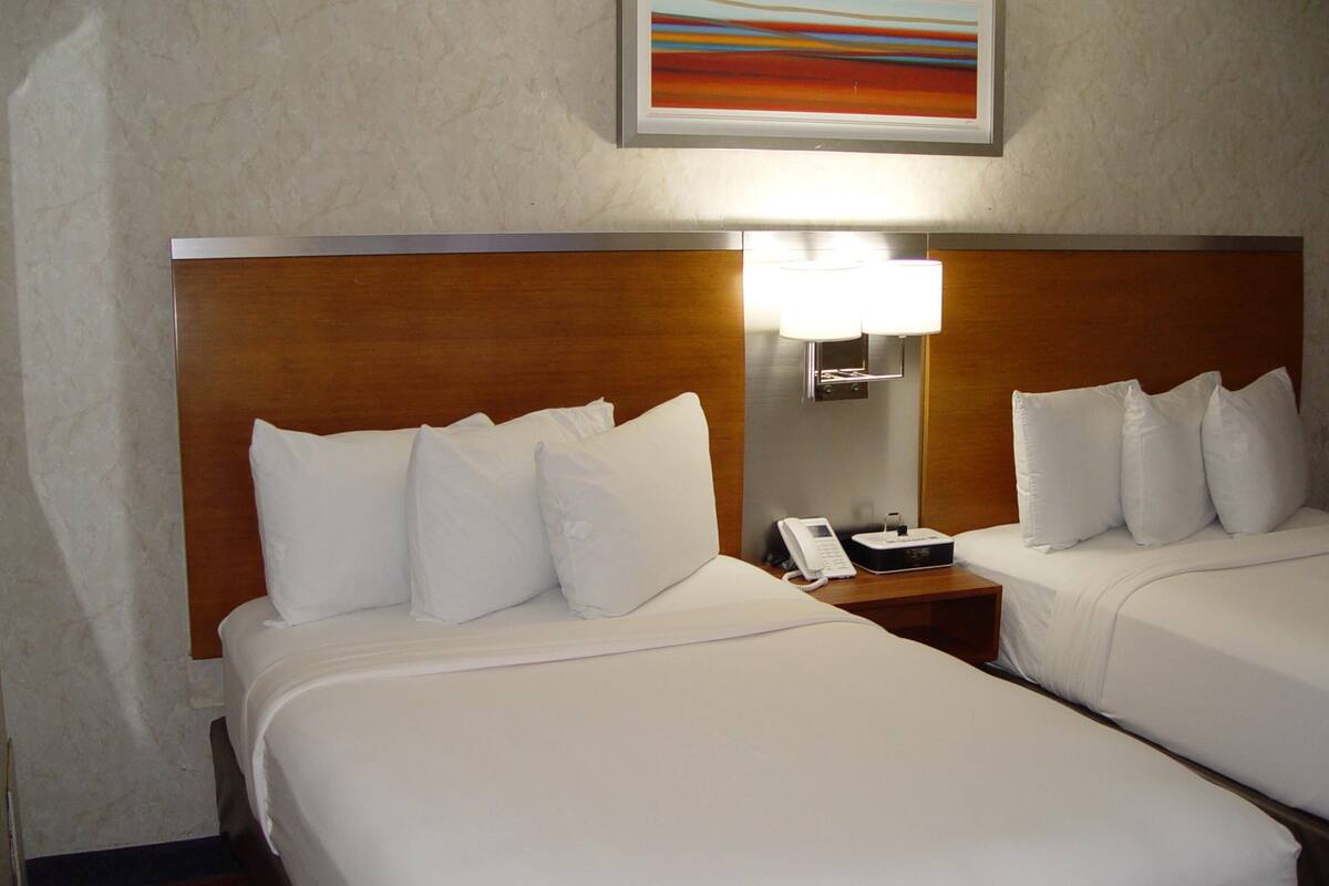 A hotel room with two beds, a nightstand with a phone, and a wall-mounted lamp.