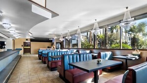 A restaurant with booths and tables, large windows, and a view of palm trees.