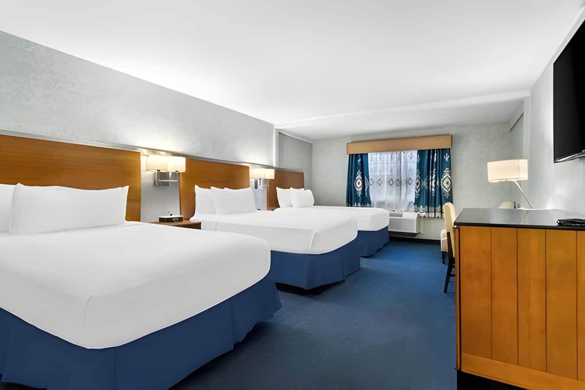 A hotel room with two beds, a desk, a chair, a TV, and a window with curtains.