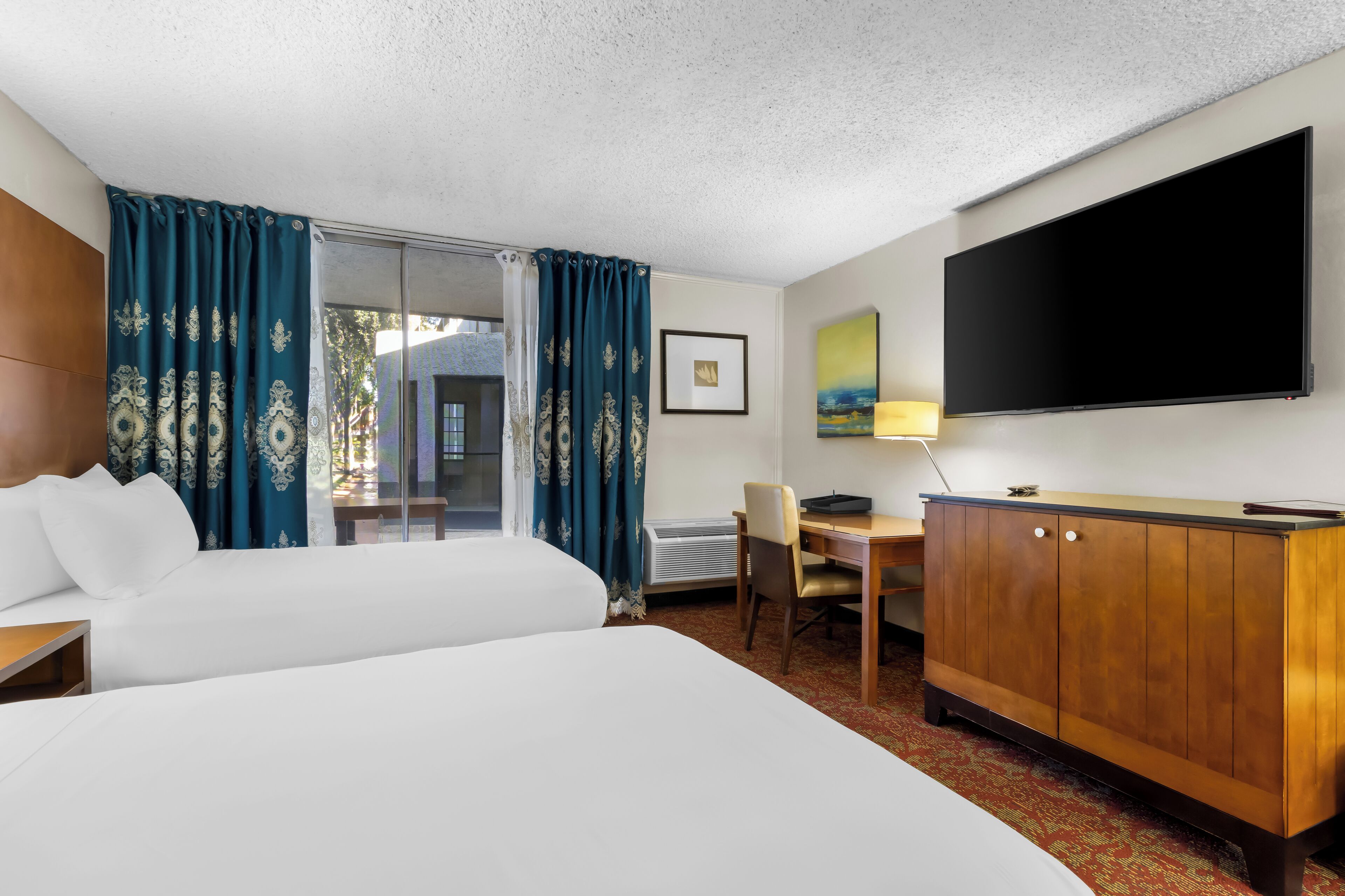 Ein Hotelzimmer mit einem großen Bett, einem Schreibtisch, einem Sessel, einem Fernseher und einem Kleiderschrank.