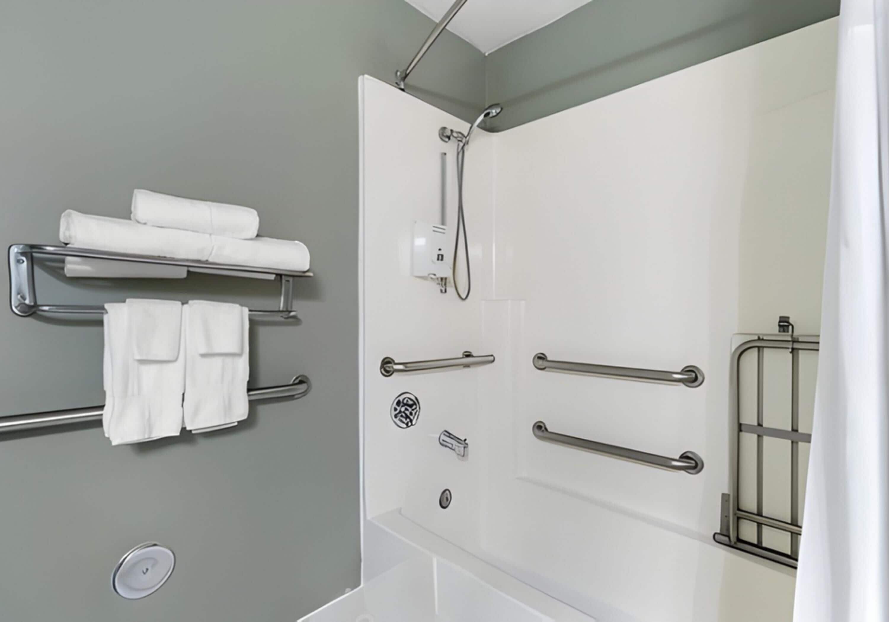 A bathroom with a shower, grab bars, a towel rack, and a toilet paper holder.