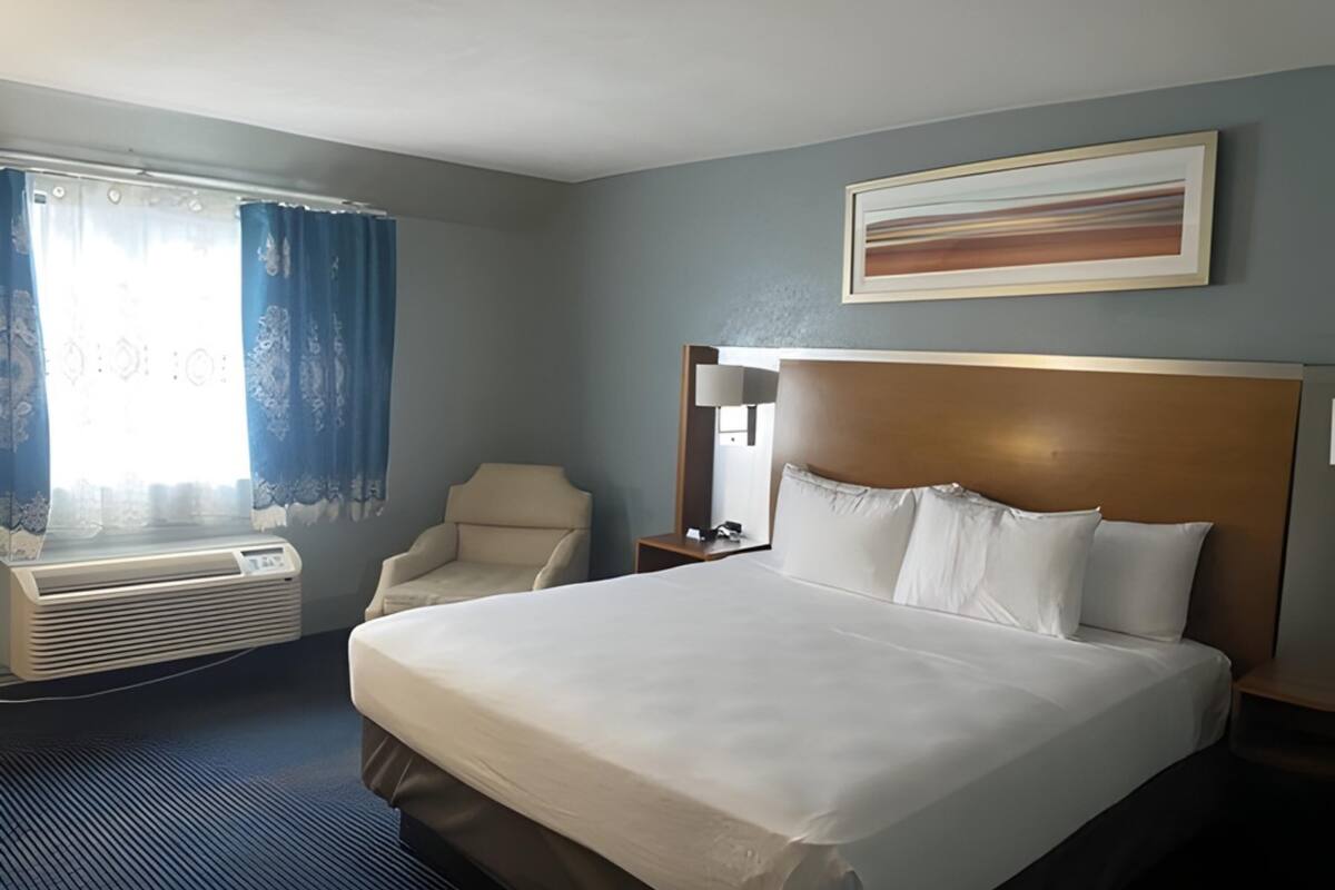 A hotel room with a large bed, a chair, a desk, and a window with curtains.