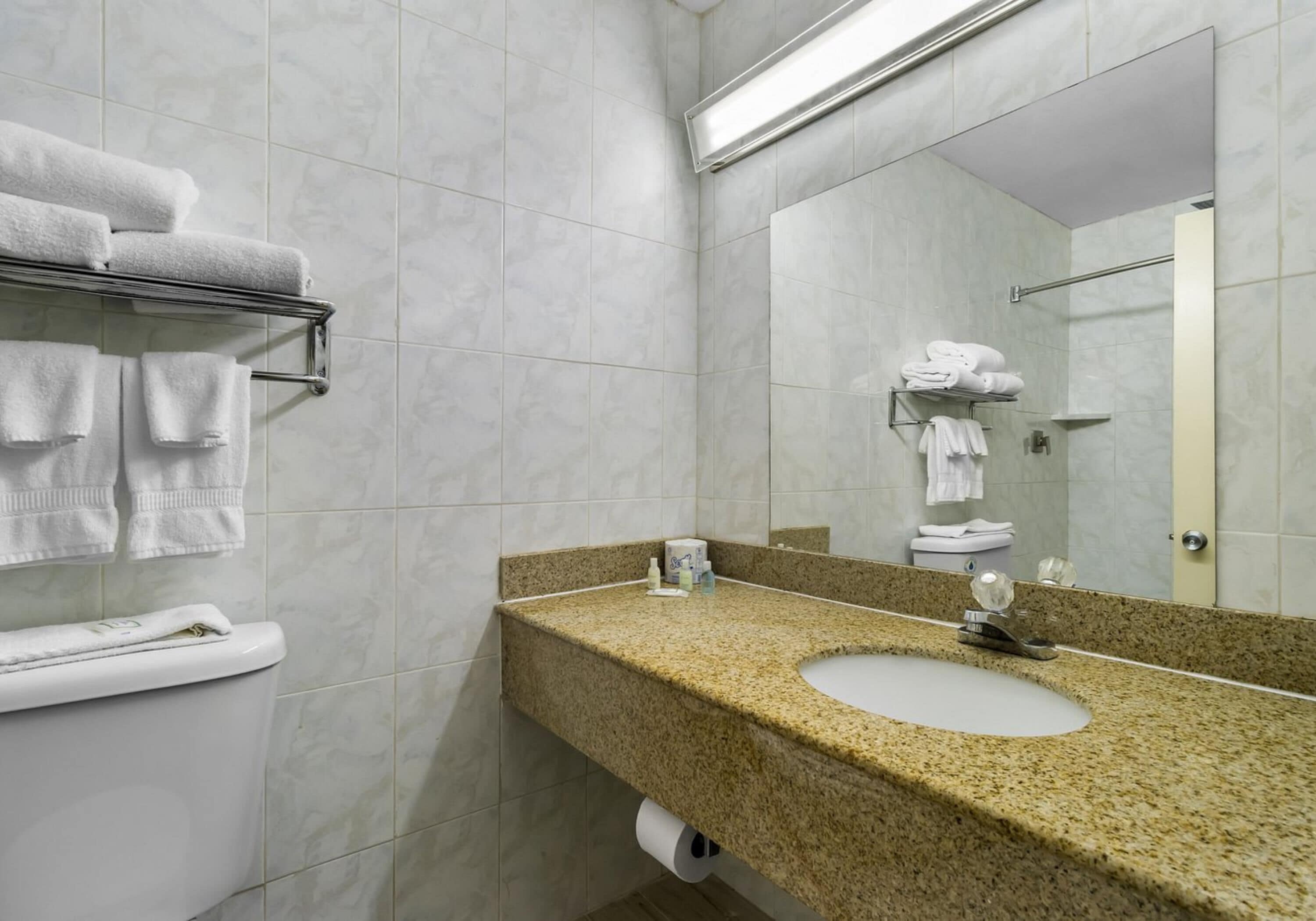 Un baño con inodoro, lavamanos, espejo, toallero y dispensador de toallas.