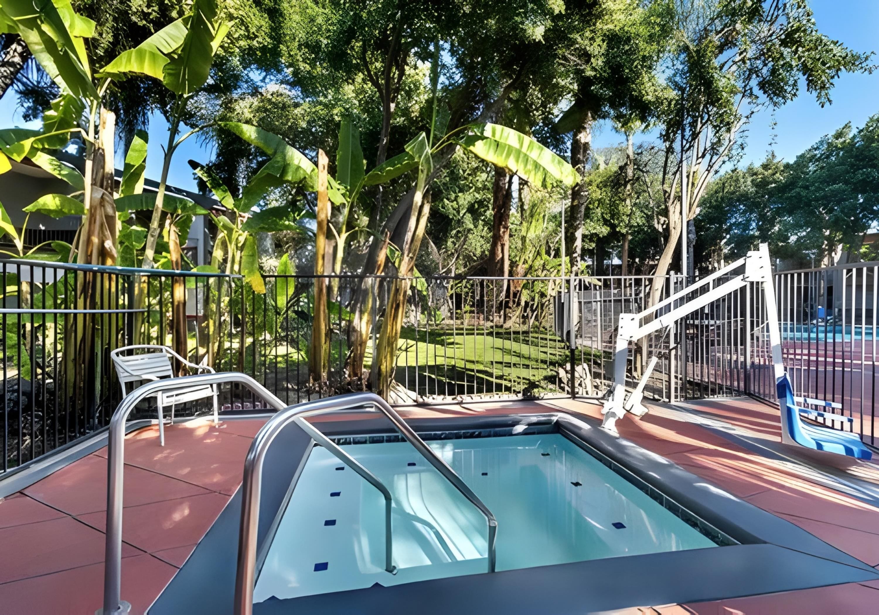 Une piscine avec un escalier en métal, entourée d’une clôture, et des chaises blanches à proximité.