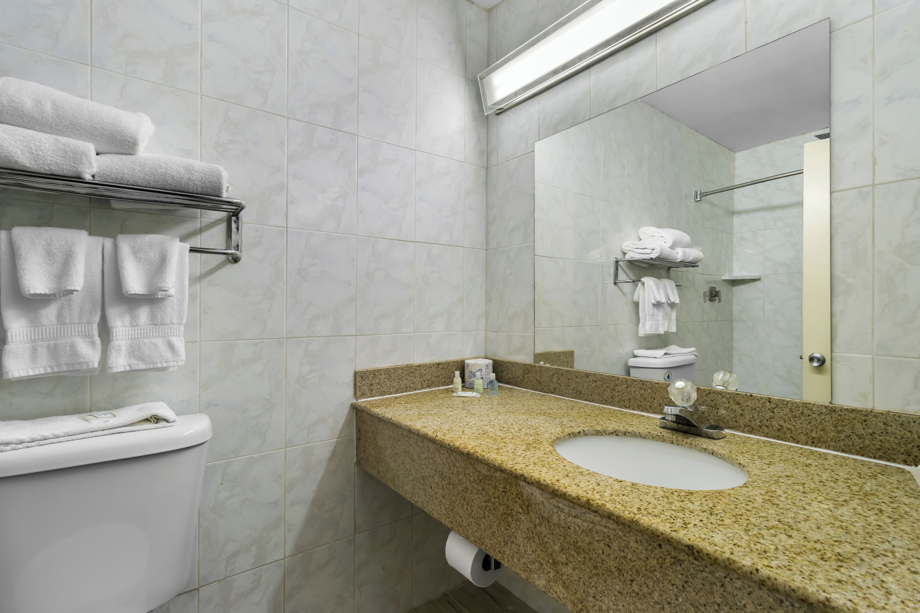 Un baño con lavamanos de encimera de granito, azulejos blancos, un perchero y un espejo.