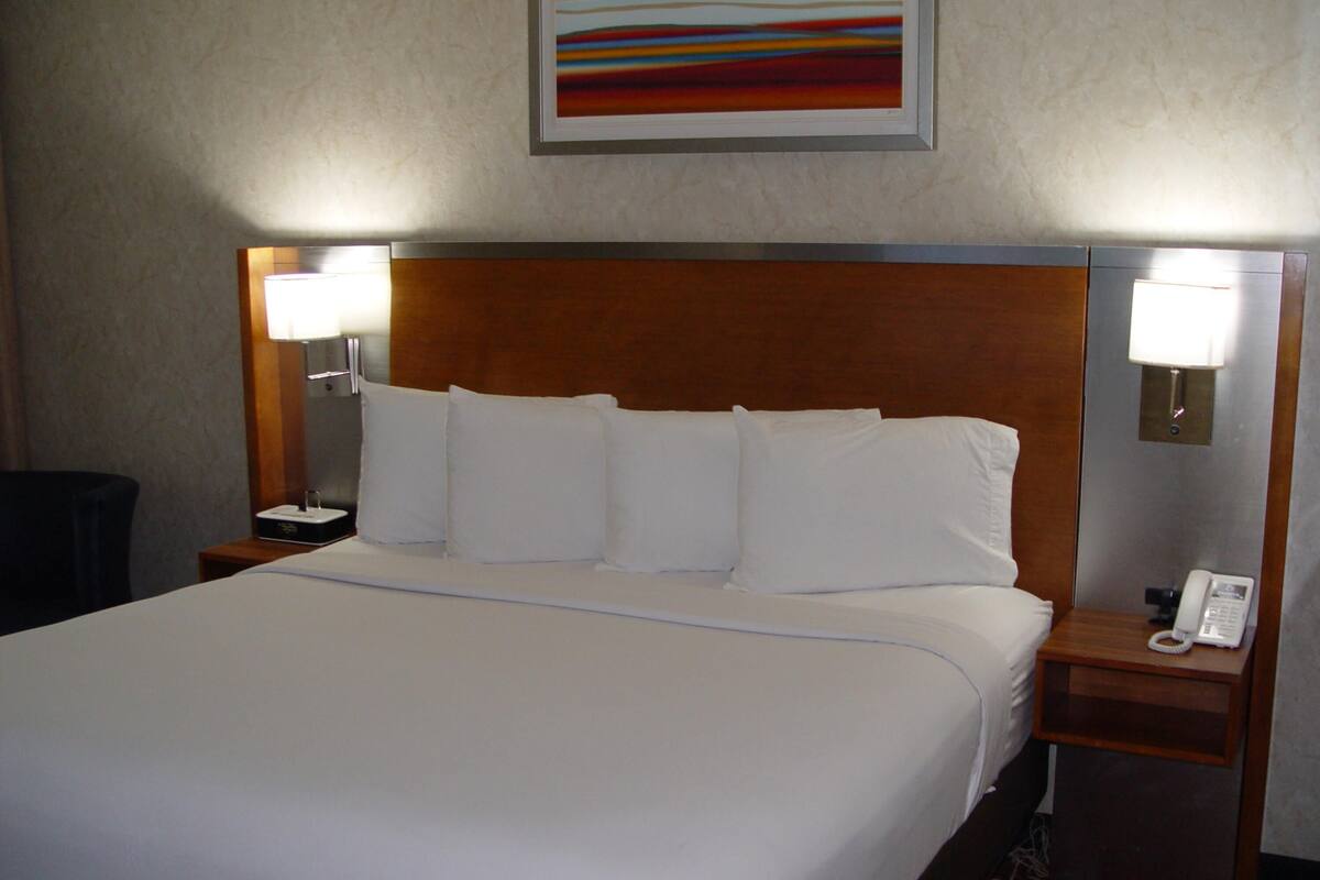 A hotel room with a large bed, two bedside tables, a lamp on each table, and a painting on the wall.
