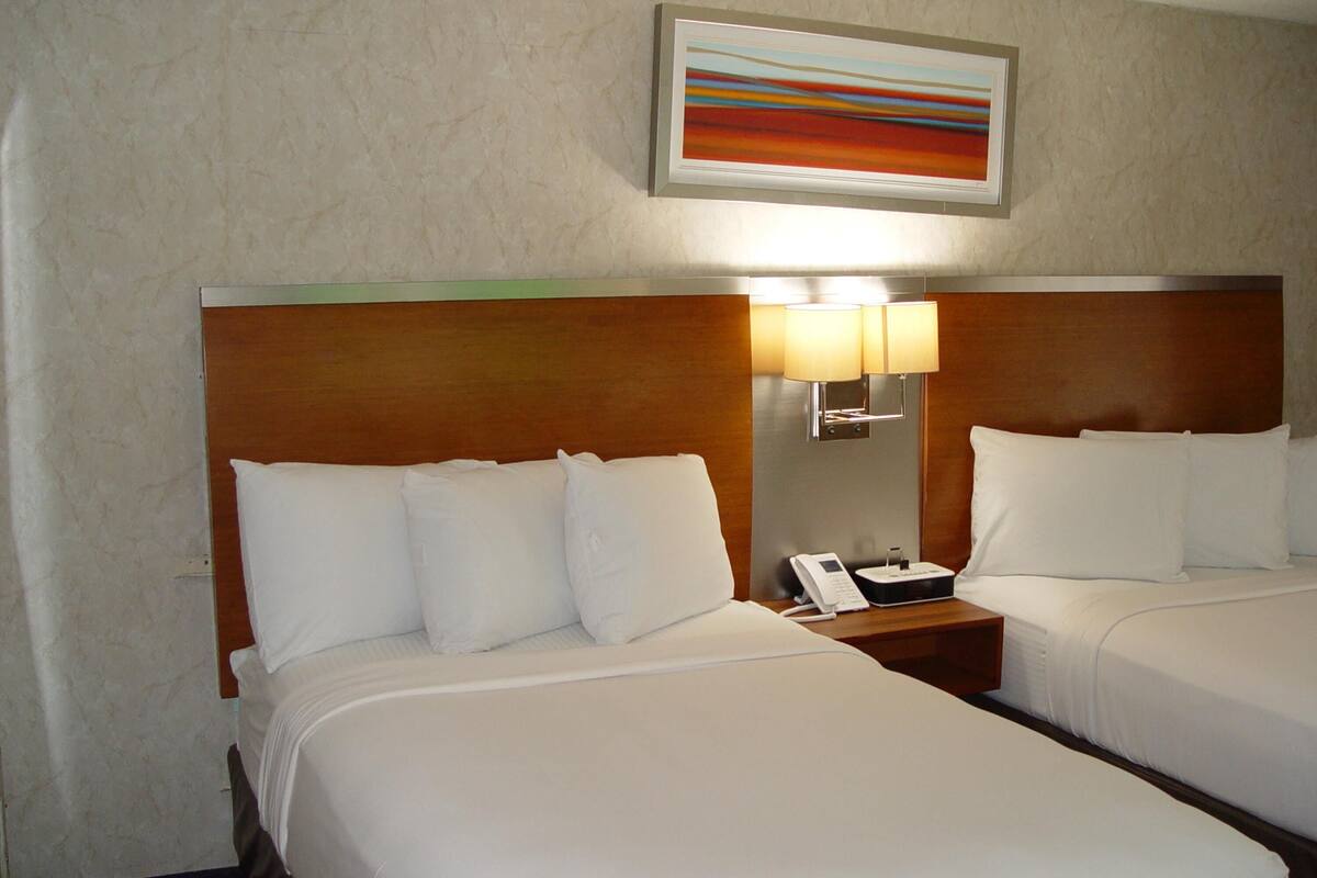 A hotel room with two beds, a nightstand with a phone, and a wall-mounted lamp.