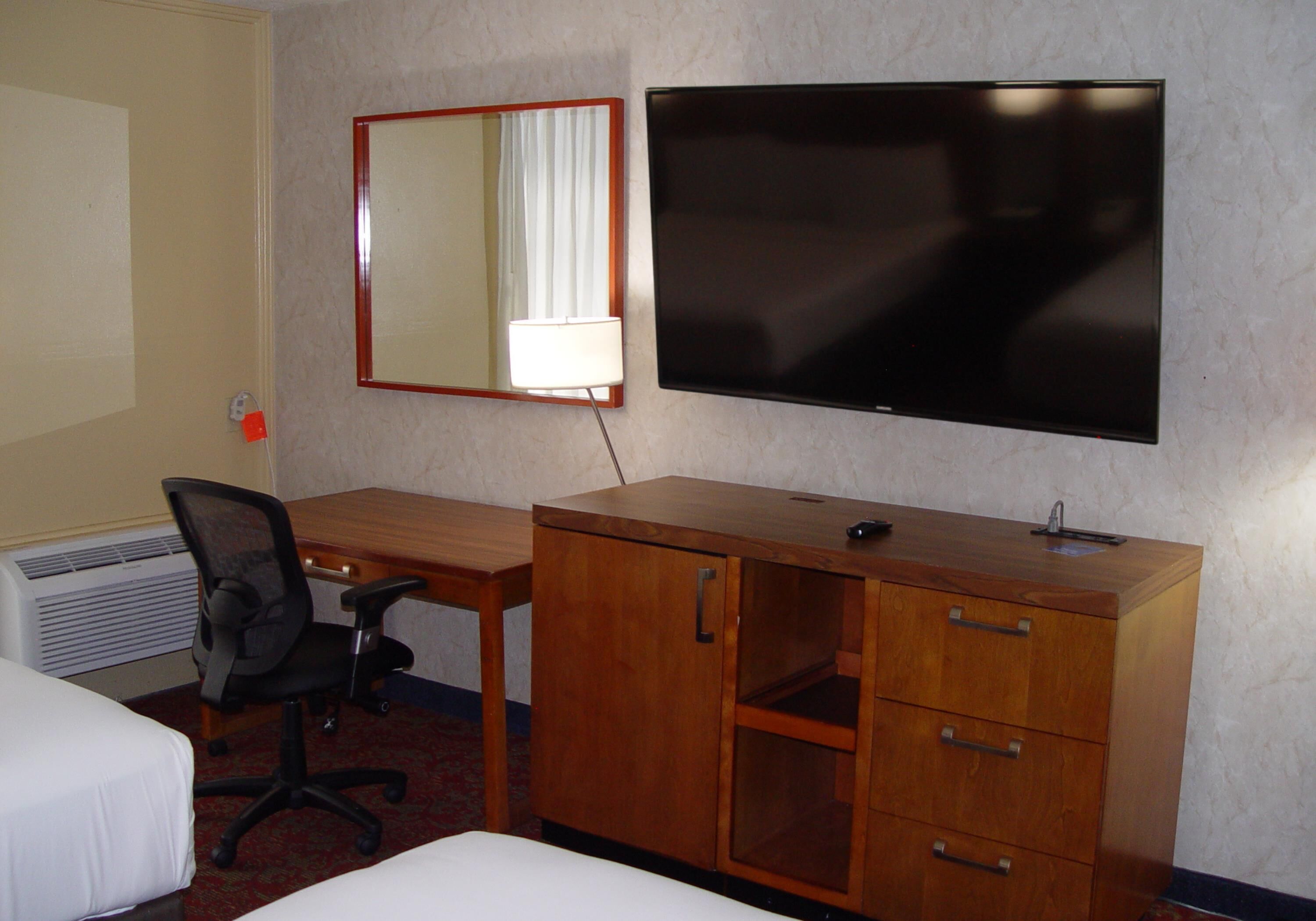 Een hotelkamer met een bed, een bureau, een stoel, een dressoir, een televisie en een spiegel.