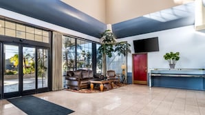 A spacious lobby with a seating area, a large plant, a flat-screen TV, and a reception desk.