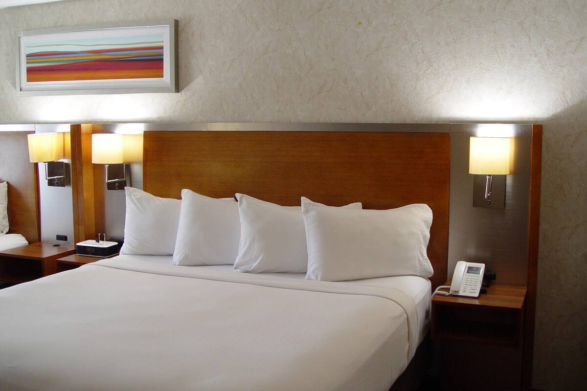 A hotel room with a large bed, two bedside lamps, a nightstand with a phone, and a painting on the wall.