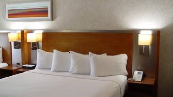 A hotel room with a large bed, two bedside lamps, a nightstand with a phone, and a painting on the wall.