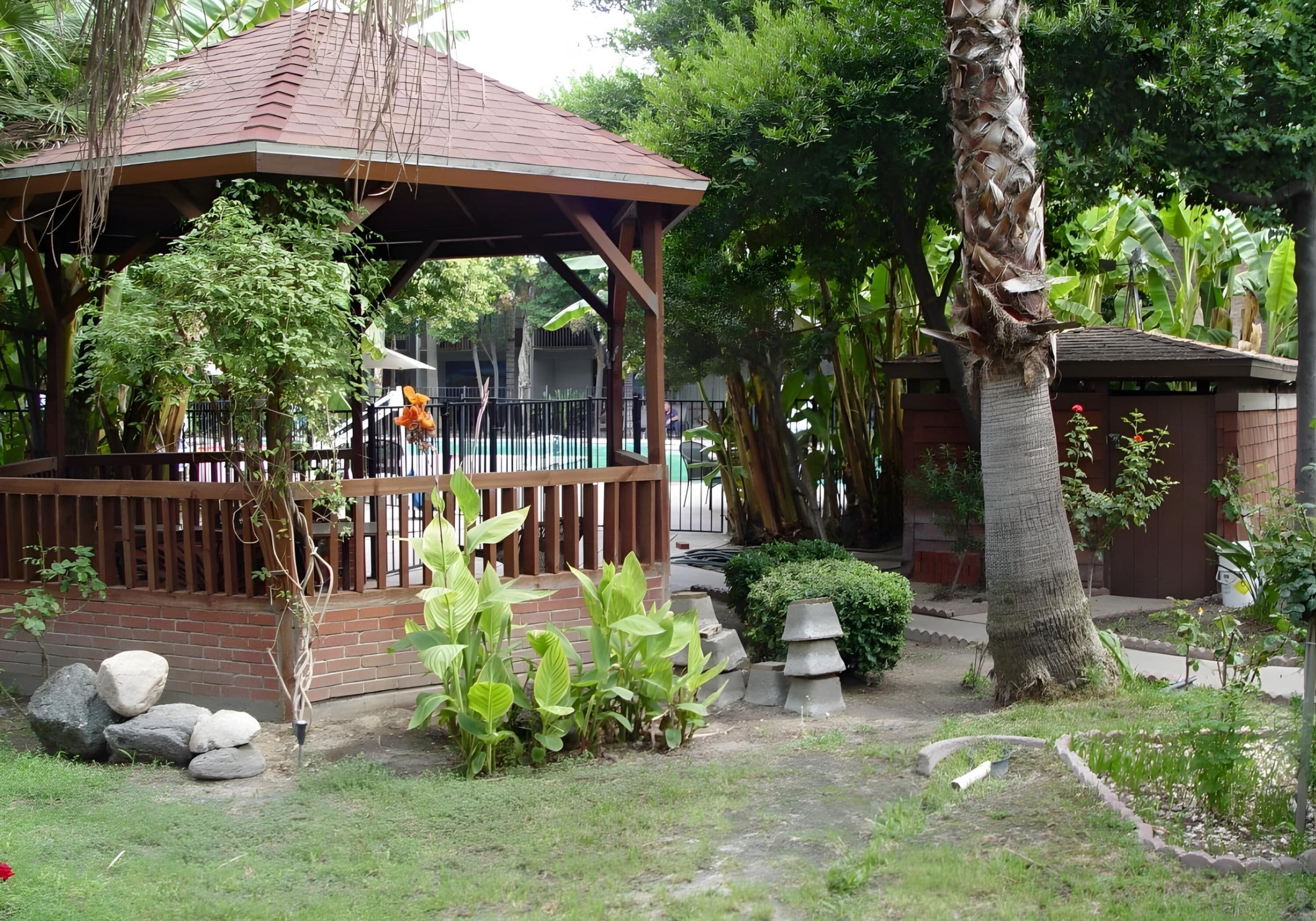 A gazebo with a tiled roof, surrounded by lush greenery and a brick wall.