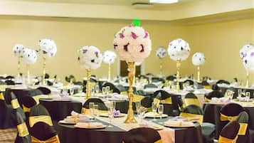 A banquet hall with round tables, black chairs with gold sashes, and floral centerpieces on tall stands.