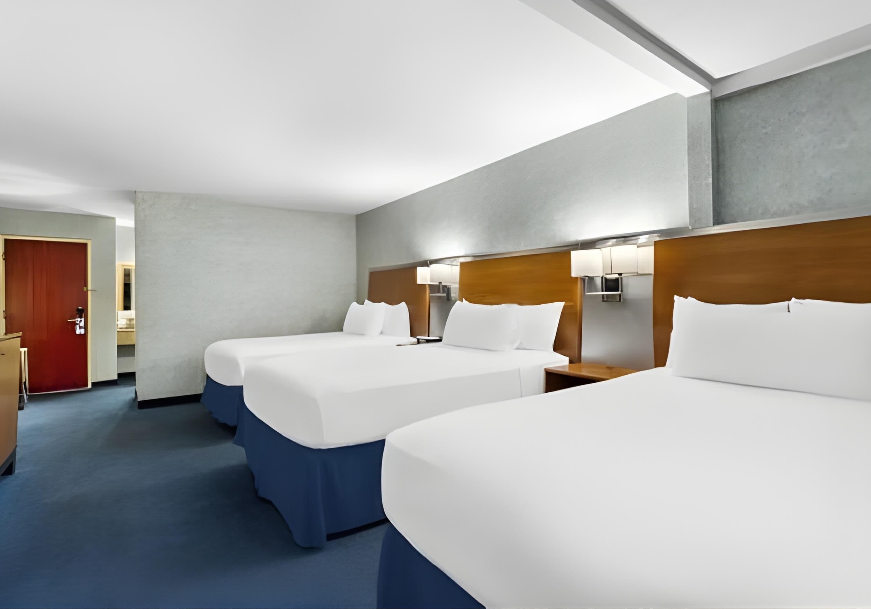 Une chambre d’hôtel avec deux lits, une tête de lit en bois, une table de chevet et une porte rouge.