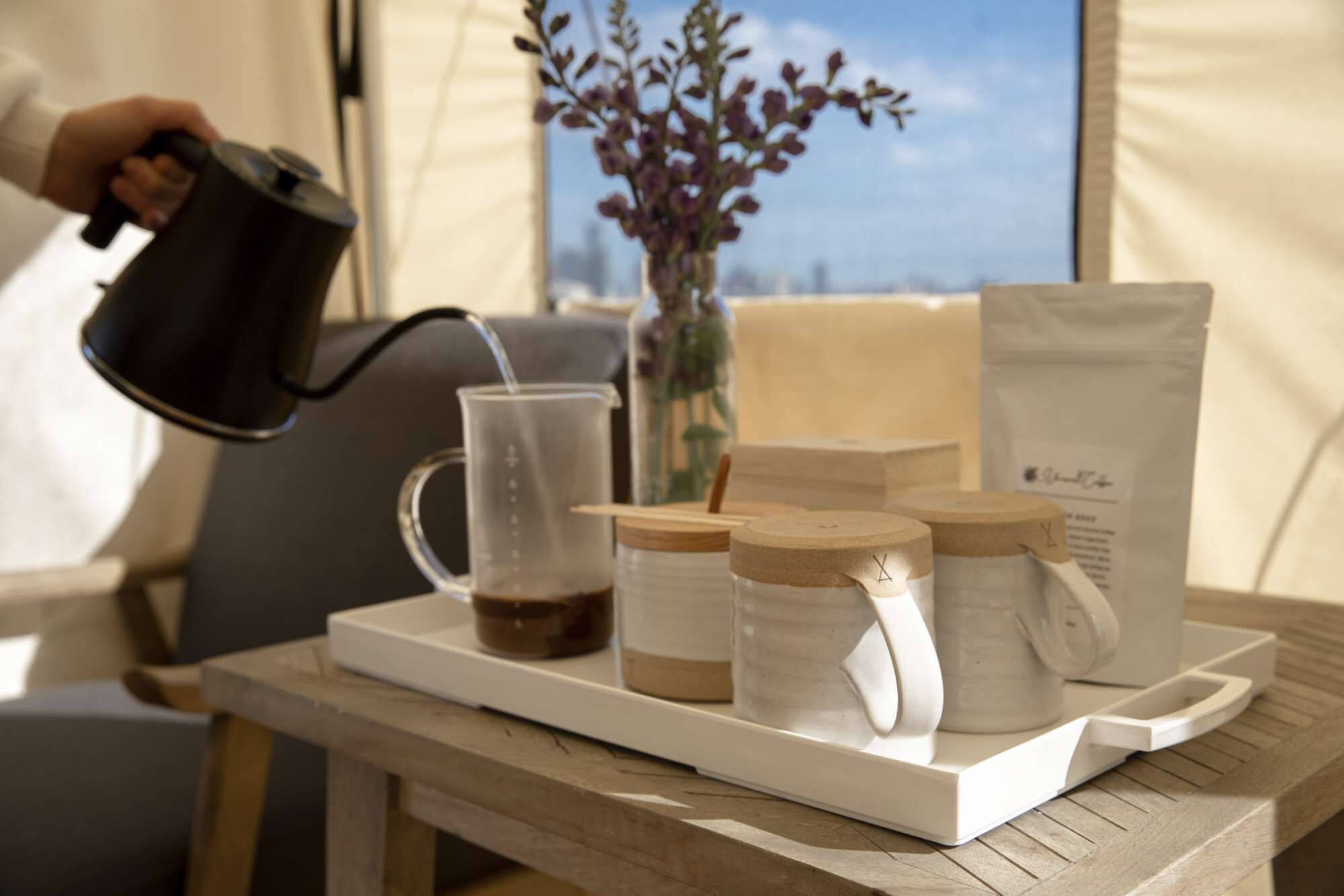 A tray with a coffee pot, a glass, and jars on a wooden table.