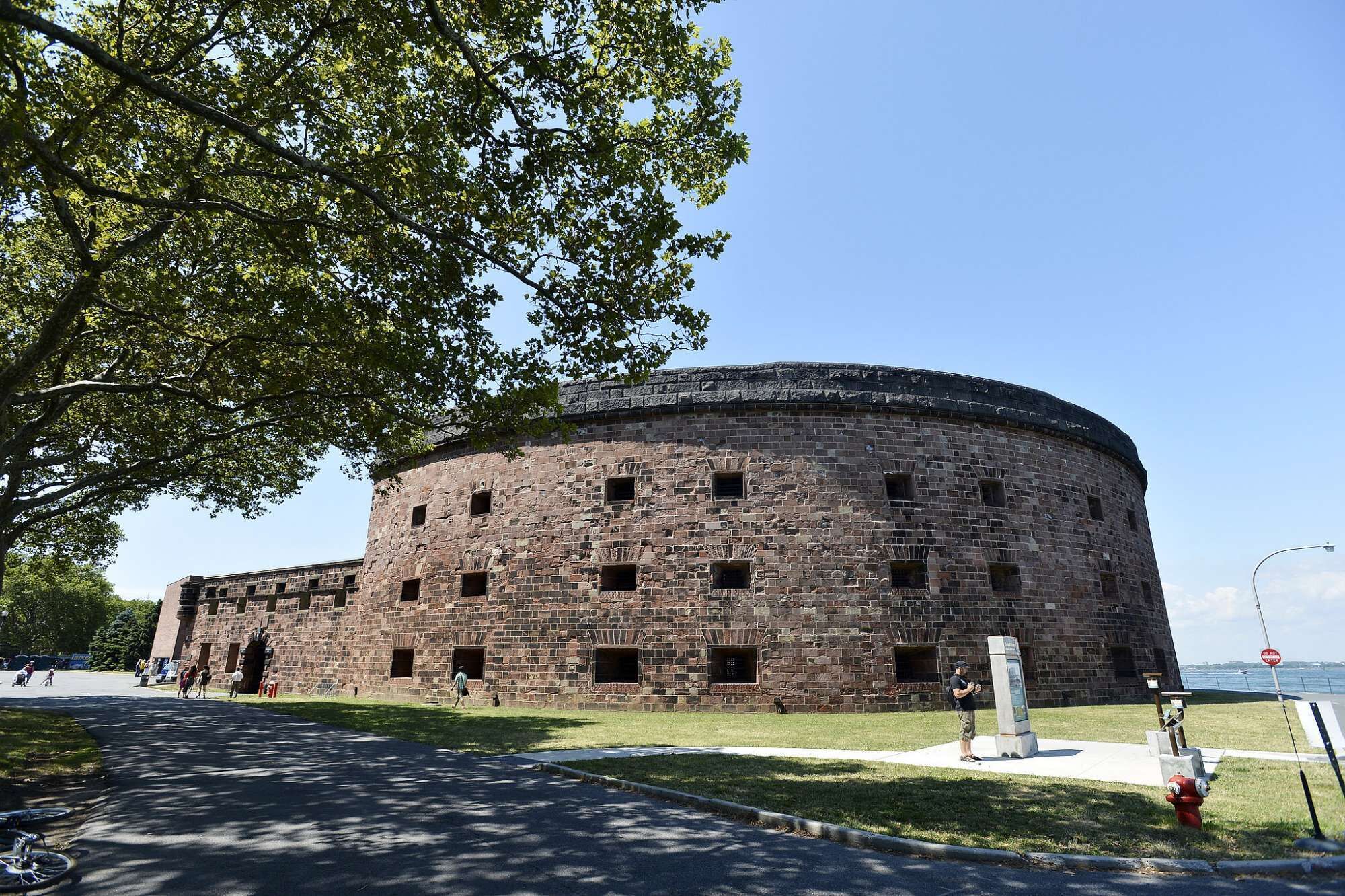 A historic stone building with a circular structure, a grassy area in front, and a clear sky.