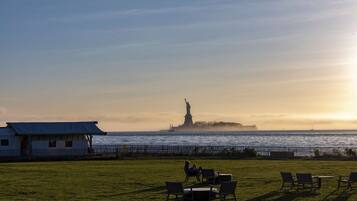A grassy area with outdoor seating, a view of the water, and a distant statue.