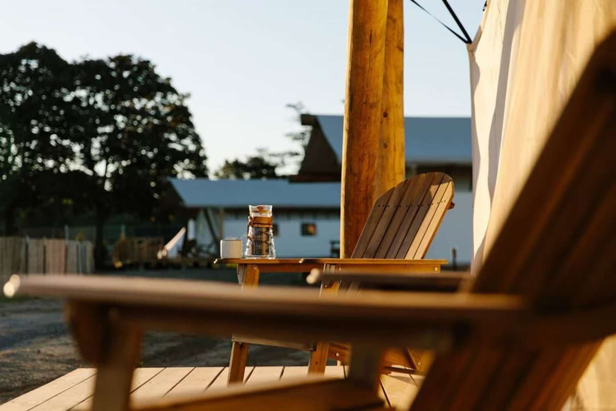 Una terraza de madera con una silla, una mesita, una botella y un vaso.