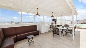 A spacious outdoor living area with a brown sofa, a dining table with chairs, a small kitchen area, and a view of the sea. - Villa doña Isidora - VipVipVillas (Teguise)