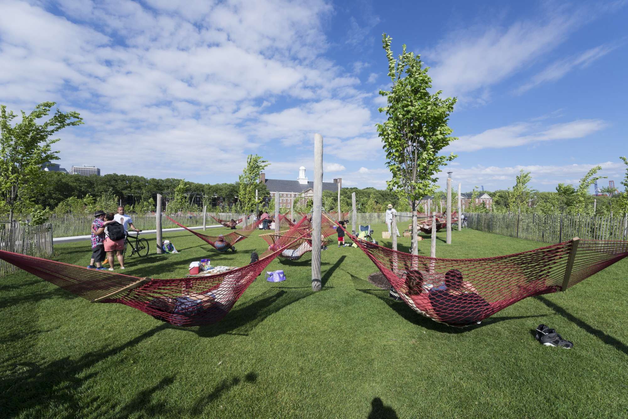 A park with green grass, red hammocks, and trees.