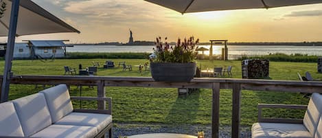 En terrasse med udendørs siddepladser, udsigt til Frihedsgudinden og en solnedgang over vandet.