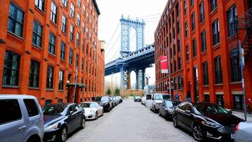 A street lined with red brick buildings, parked cars, and a bridge in the background.