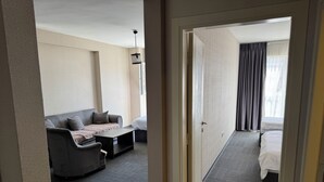 A hotel room with a sofa, a small table, a bed, and a view of the outside through a window with curtains. - Pin Suite (Istanbul)