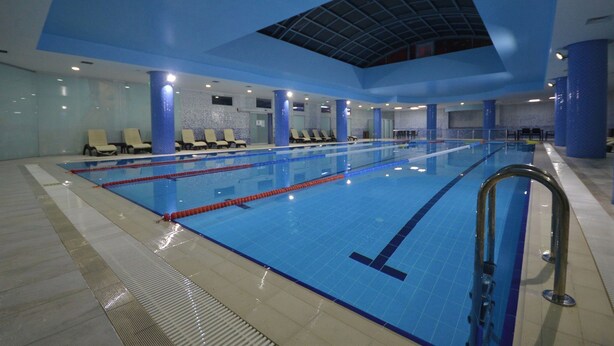 An indoor swimming pool with clear lanes, blue-tiled floor, and a high ceiling with a skylight. - Pin Suite (Istanbul)