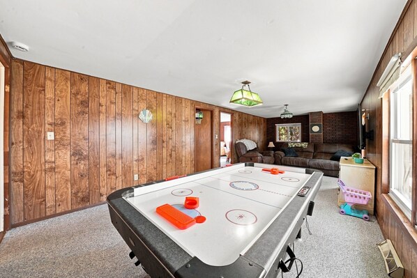 A room with a pool table, wooden walls, a sofa, and a television.