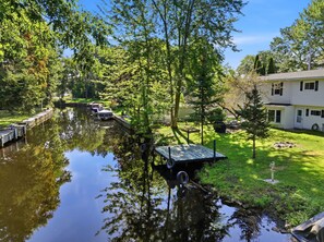 Ein ruhiger Fluss mit einem Steg, umgeben von üppiger Vegetation und einem Haus.