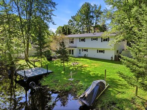 Une maison à deux étages avec un jardin devant, un petit quai et un étang.